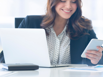 Woman at computer looking at her phone