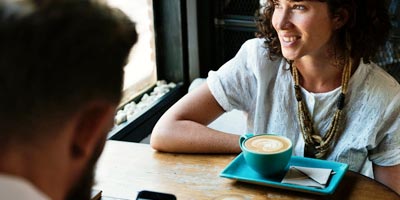 A woman sits across from a companion drinking a coffee